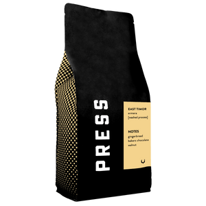 A Black "PRESS" coffee bag with writing on a yellow label
