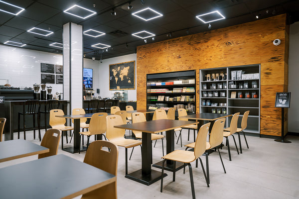 Moden, sleek looking wooden tables and chairs are set by a back drop of bags of whole bean coffee, a world map of the coffee belt, and more. 