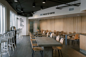 An interior photograph of Press Coffee Skywater location. Featuring modern looking tables and chairs with a wood-finished wall. 